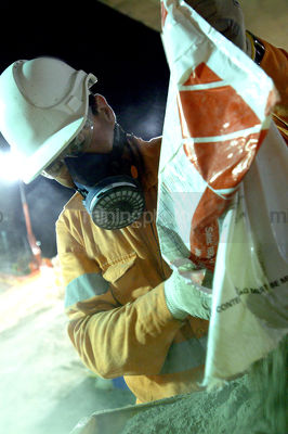 Construction worker wearing a safety mask works with concrete bags at night.  vertical shot. - Mining Photo Stock Library