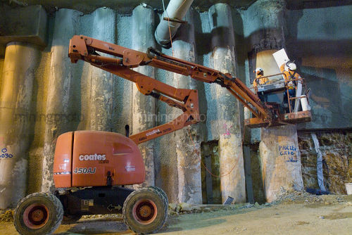Two construction workers on mobile cherry picker in underground tunnel fit form work to concrete posts. - Mining Photo Stock Library