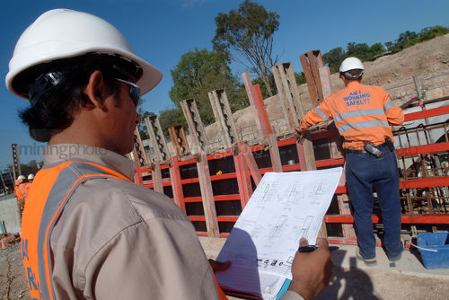 Site supervisor in hard hat with clipboard of plans checks over site workers. - Mining Photo Stock Library
