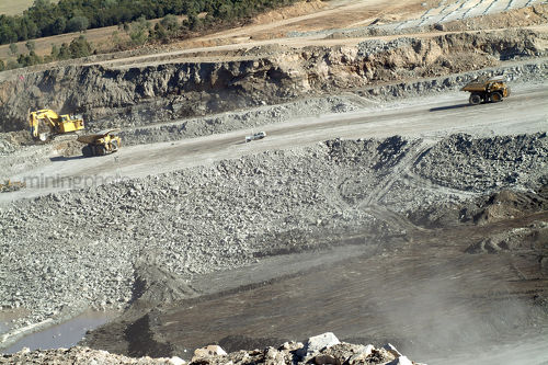 Aerial shot of open cut coal mine with 2 truck rotation, excavator loading and small light vehicle in there for scale.  blasting setup hole sin background. - Mining Photo Stock Library