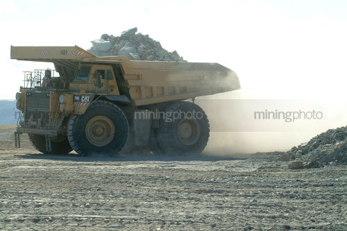 Fully loaded haul truck on open cute mine site arrives to dump overburden. pile of dust. - Mining Photo Stock Library