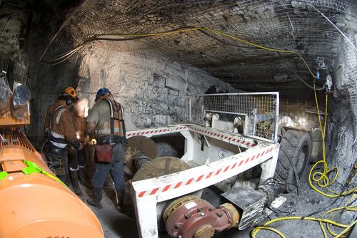 Three underground coal miners working together to attach cable to machinery with specialised mine vehicle close by. - Mining Photo Stock Library