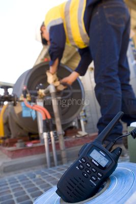 Radio walkie talkie up close with worker out of focus in background. iniden signage can be removed. - Mining Photo Stock Library