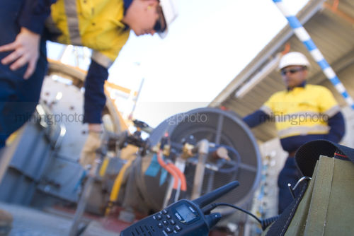 Two workers on mine site with radio walkie talkie shot in foreground in focus. - Mining Photo Stock Library