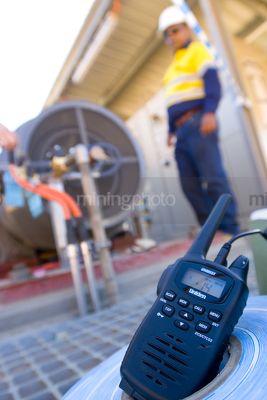 Radio walkie talkie up close with worker out of focus in background. iniden signage can be removed. - Mining Photo Stock Library