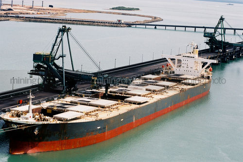 Coal ship being loaded at terminal with long jetty, wharf and coal stockpile in background. - Mining Photo Stock Library
