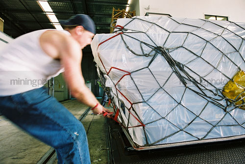 Factory workers tying down plane cargo awaiting export. - Mining Photo Stock Library
