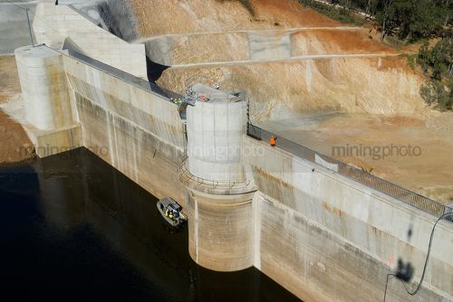 Workers finishing dam wall construction.  man in PPE on top and others in boat on the water. great wide water and dam wall shot. - Mining Photo Stock Library