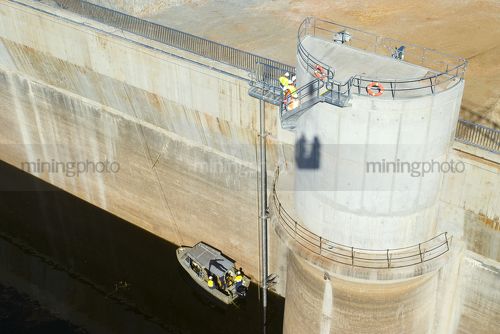 Workers finishing dam wall construction.  man in PPE on top and others in boat on the water. aerial shot - Mining Photo Stock Library