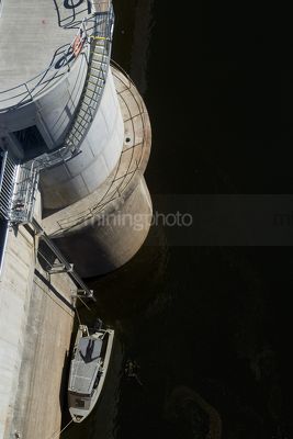Dam wall with maintenance boat parked alongside and scuba diver worker in water.
aerial, vertical shot. - Mining Photo Stock Library