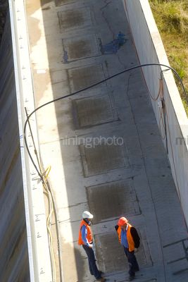 Two workers in discussion on top of a dam wall. aerial vertical shot. - Mining Photo Stock Library