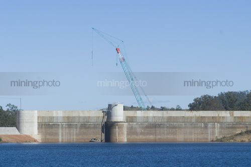 Construction crane working on a dam wall. shot from the water side with a maintenance boat at the base of the wall. - Mining Photo Stock Library