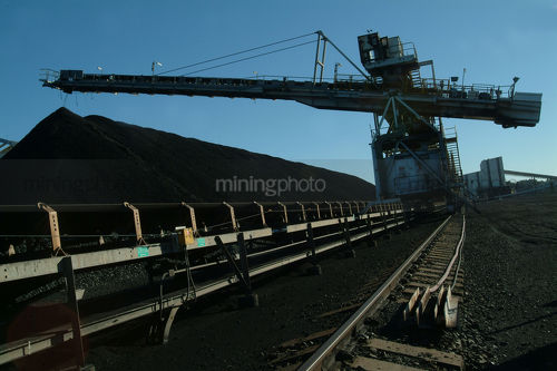 Moving conveyor with a coal loader stockpiling in the background. shot late in the day and could be a  silhouette. - Mining Photo Stock Library