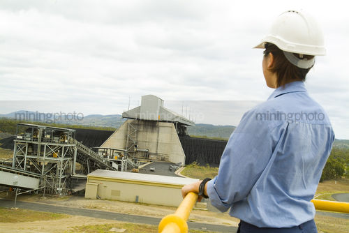 Female worker at power station looking out to hopper where coal is being loaded onto conveyor. - Mining Photo Stock Library