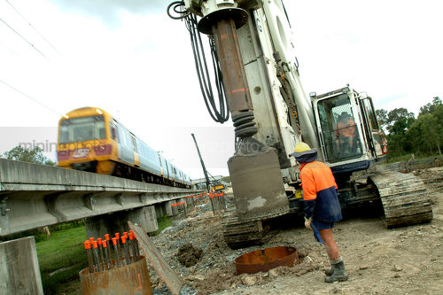 Worker drilling pylons  net to QLD light Rail infrastructure track duplication project. train passing by.  great shot. - Mining Photo Stock Library