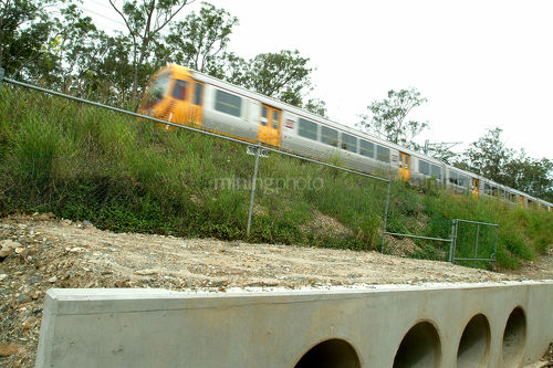 Light rail passenger train passing over culvert with landscaped bank in middle ground. - Mining Photo Stock Library