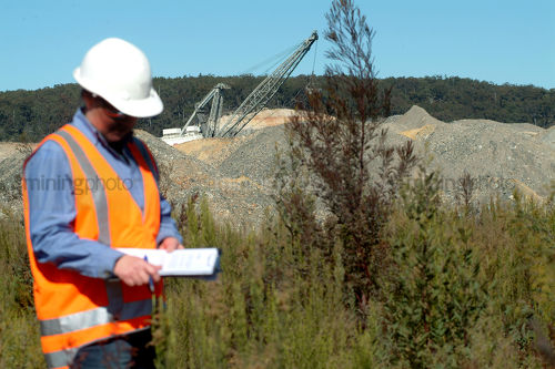 Environmental officer on open cut mine site inspecting planting. dragline in pit behind. - Mining Photo Stock Library