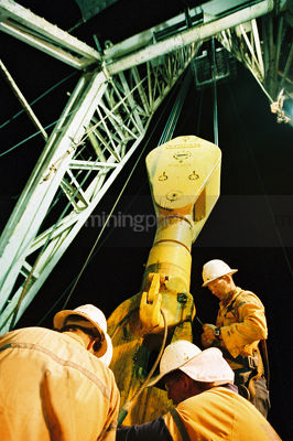 Workers in PPE inspecting the derrick on a drill rig.  shot at night and looking up the derrick for full height.  vertical shot - Mining Photo Stock Library