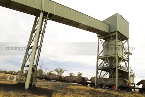 Heavy rail carriages being loaded with coal by overhead hopper and conveyor. - Mining Photo Stock Library