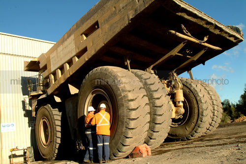 Workers in PPE servicing a lare coal haul truck.  shot from the rear for maximum scale. - Mining Photo Stock Library