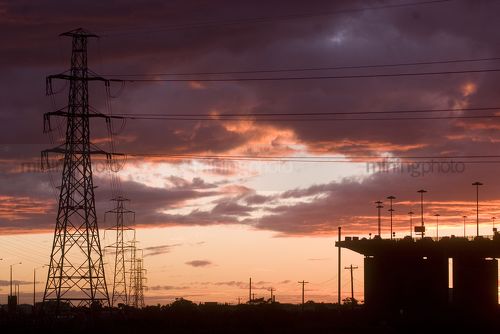 Sunset Silhouette image of traffic moving on large bridge. giant powerlines nearby. great colour in sky. - Mining Photo Stock Library