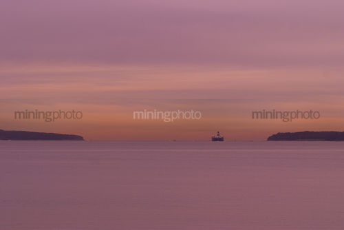 Container ship moving through headlands in the distance.  lots of ocean and great susnet colours.  lots of area for design element or text. - Mining Photo Stock Library