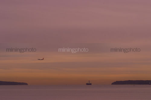 Container ship moving through headlands in the distance.  domestic plane flying in low to land at airport.  lots of ocean and great susnet colours.   - Mining Photo Stock Library