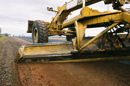 Grader working the shoulder of a road.  shot from ground level. - Mining Photo Stock Library