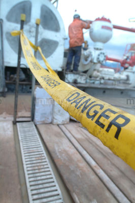 Oil and gas rig worker on general mine site in background with DANGER roped off signage in foreground. good safety shot. - Mining Photo Stock Library