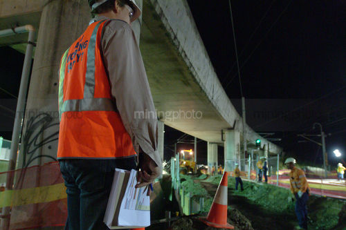 Construction manager inspecting nightworks on building site.  has pen and paper in hand and dressed in full safety ppe gear. - Mining Photo Stock Library