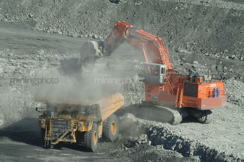 Large digger excavator loading overburden into haul truck on open cut coal mine site.  close up shot with lots of dust. aerial shot - Mining Photo Stock Library