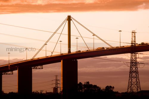 Mixture of afternoon traffic travelling along bridge with orange sky behind.  shot from the ground and close up. - Mining Photo Stock Library