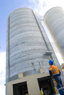 Engineer looking up at large concrete silo hopper.  vertical image shot from ground level and from behind worker. - Mining Photo Stock Library