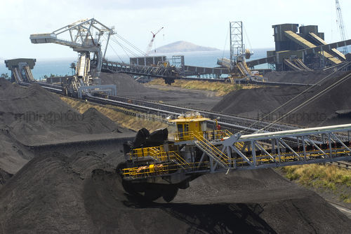 Coal reclaimers and ship loaders working at terminal with coal stockpiles and the ocean in the background. aerial shot. - Mining Photo Stock Library