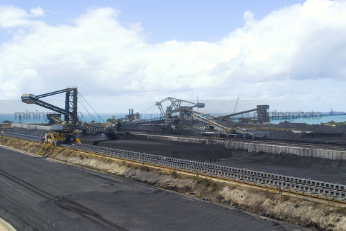 Wide panorama shot of coal terminal.  plenty of reclaimers and loaders.  long wharf out to ships being loaded  and ocean in background. great production coal panorama image. - Mining Photo Stock Library