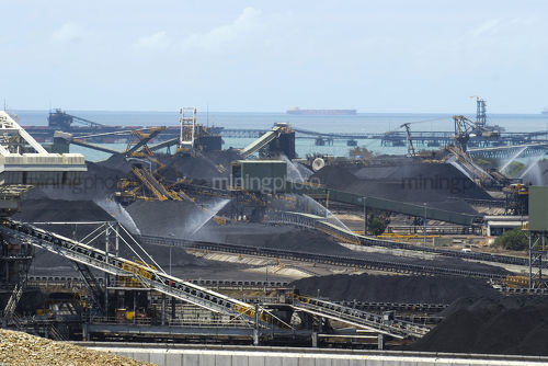 Aerial shot of coal terminal. lots of reclaimers and coal loaders, coal stockpiles and conveyors.  wharf out to ships being loaded.  ship out in the ocean in the background.  great generic coal production image.  would suit panorama or vertical. - Mining Photo Stock Library