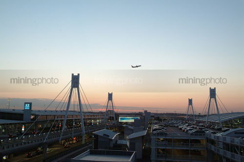 Plane taking off over T2 airport terminal at Sydney at dusk - Mining Photo Stock Library