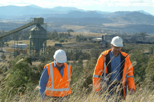 Two mine site workers inspecting revegetation on slopes above coal wash plant.  mountains, rail and plant in background. - Mining Photo Stock Library