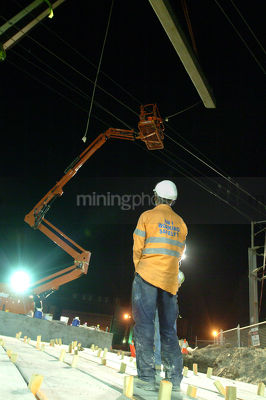 Construction worker on infrastructure site with overhead travel tower and crane lifting steel beams. - Mining Photo Stock Library