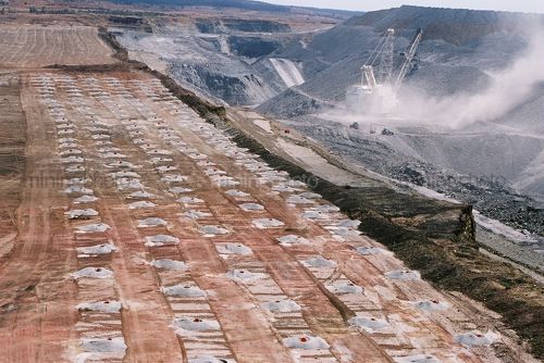 Dragline in open cut coal mine removing overburden.  blasting holes drilled and filled in foreground.  aerial image. - Mining Photo Stock Library