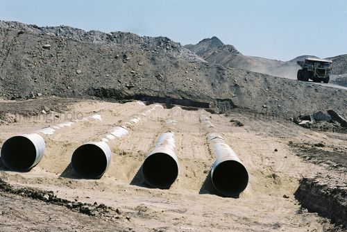 Water pipes under opencut haul road with large mine truck driving past - Mining Photo Stock Library