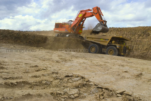 Digger and haul truck removing overburden in open cut coal mine.  truck and digger are out of focus.  good generic coal action image.  lots of dust and can see the benches. - Mining Photo Stock Library