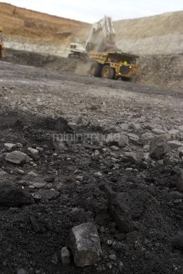 Close up of coal in open cut coal mine with wide dramatic background to out of focus haul truck and digger.  vertical image. - Mining Photo Stock Library