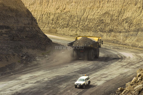 Loaded haul truck passes light vehicle on haul road out of the floor of open cut mine. - Mining Photo Stock Library