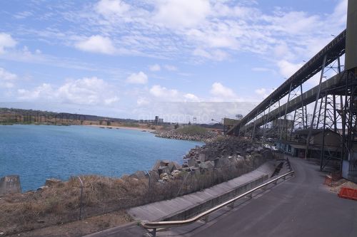 Conveyor at coal terminal passing next to ocean and site fence. - Mining Photo Stock Library