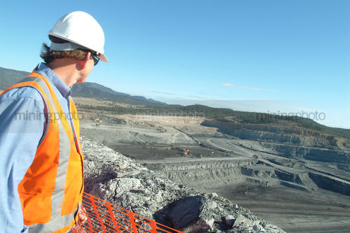 Mine site engineer in full ppe looking out over open cut coal mine from high point. - Mining Photo Stock Library