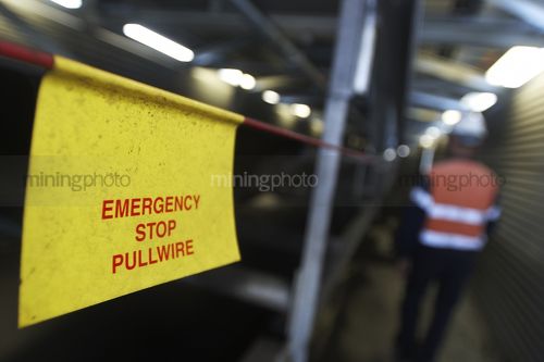 Emergency stop pullwire  
next to coal conveyor with mine worker in background. - Mining Photo Stock Library