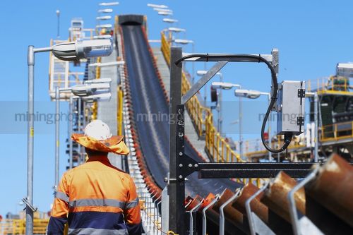 Mine worker with sun protection hat walking next to coal conveyor - Mining Photo Stock Library