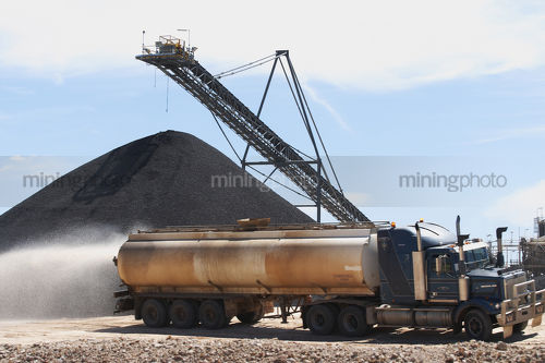 Large truck water cart spraying water with coal stockpile in background. - Mining Photo Stock Library