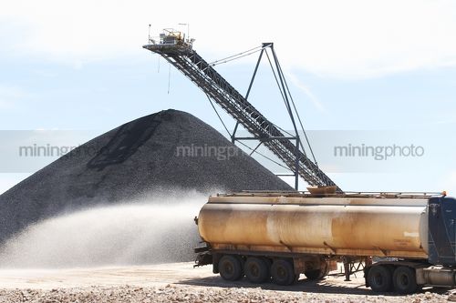 Water cart spraying water with coal stockpile in background. - Mining Photo Stock Library